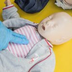 A person demonstrates infant CPR on a manikin, highlighting first aid techniques.