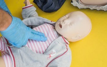 A person demonstrates infant CPR on a manikin, highlighting first aid techniques.