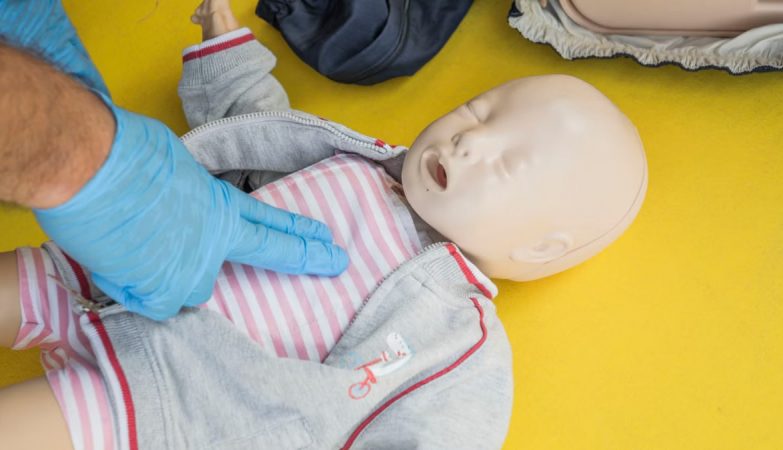 A person demonstrates infant CPR on a manikin, highlighting first aid techniques.